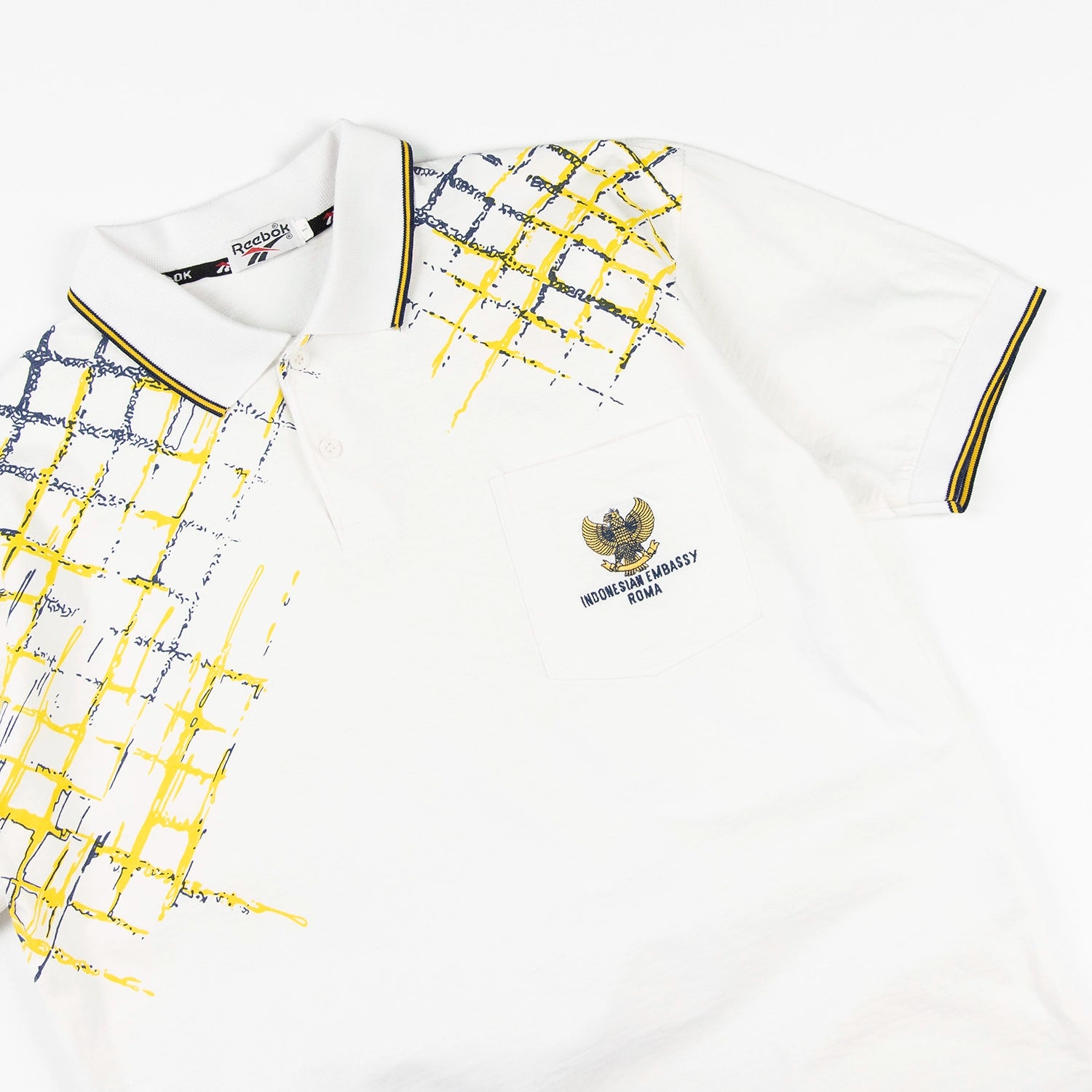 Polo vintage Reebok con grafica gialla e blu e logo Indonesian Embassy Roma sul petto